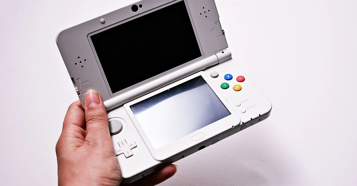 Gros plan d'une main tenant une console de jeu portable ouverte, avec deux écrans.