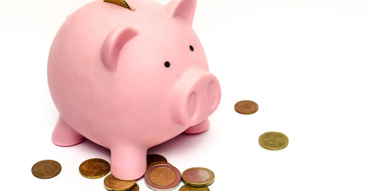Une tirelire rose entourée de pièces éparpillées, symbolisant les économies et l'investissement financier.